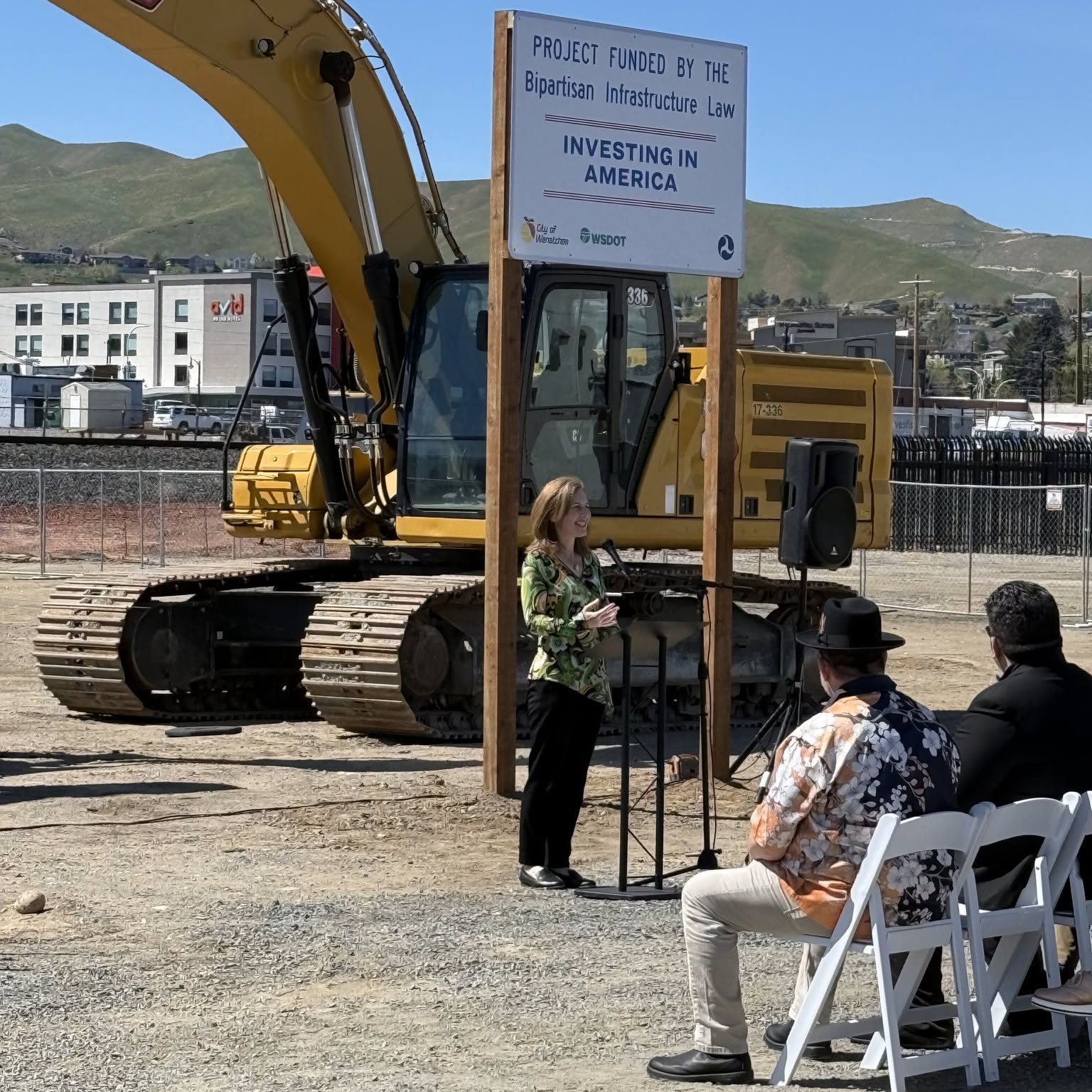 Speaker addressing guests seated in white folding chairs at a construction groundbreaking ceremony