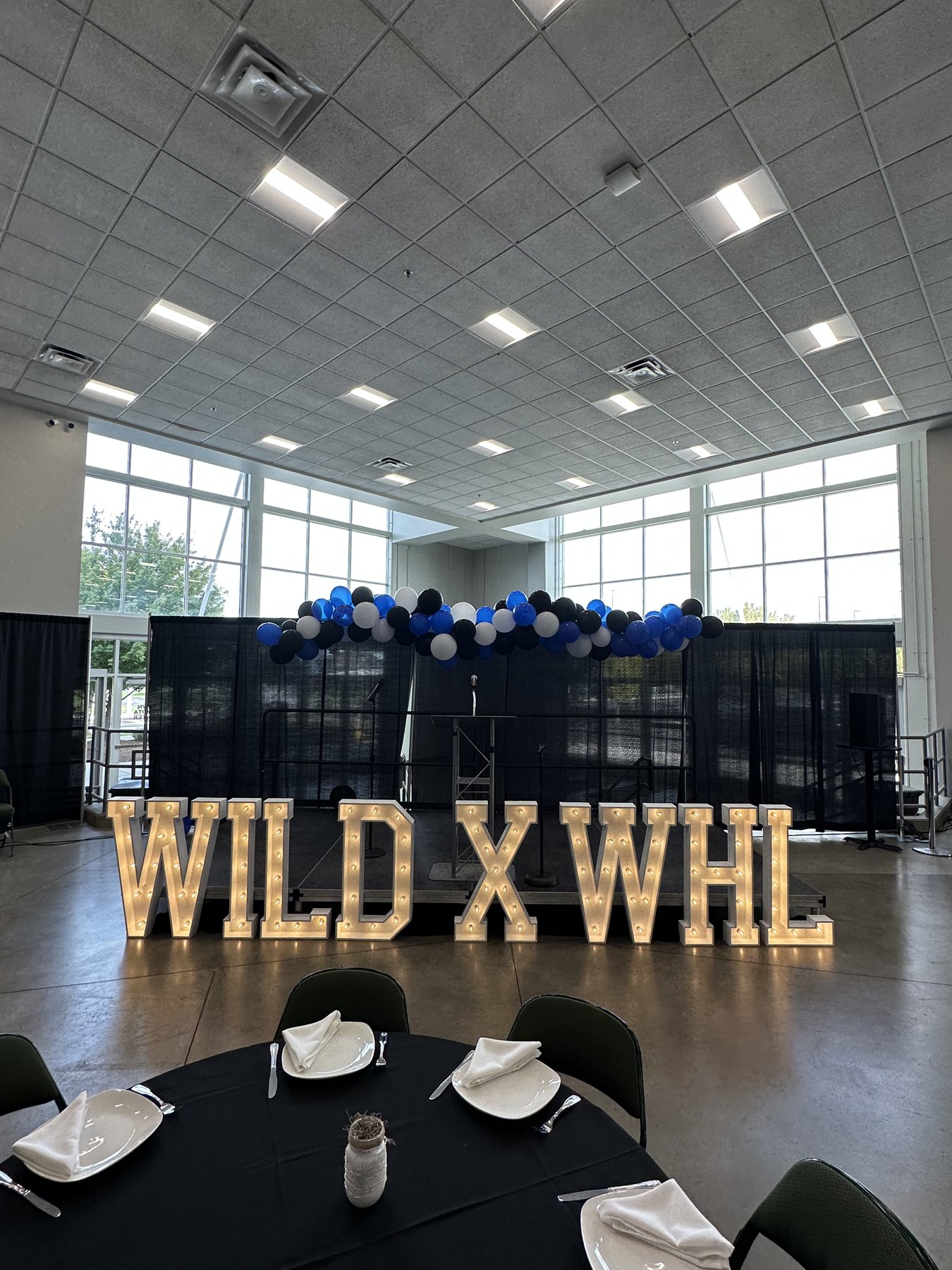 Illuminated WILD X WHL marquee letters with balloon garland and banquet tables at a corporate hockey partnership event