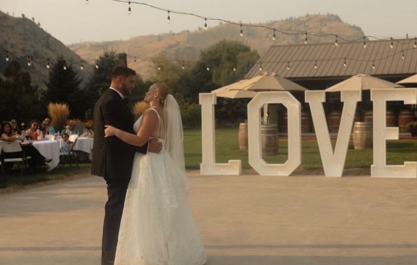 Newlyweds dancing in front of illuminated LOVE marquee letter rentals at a vineyard wedding in Eastern Washington