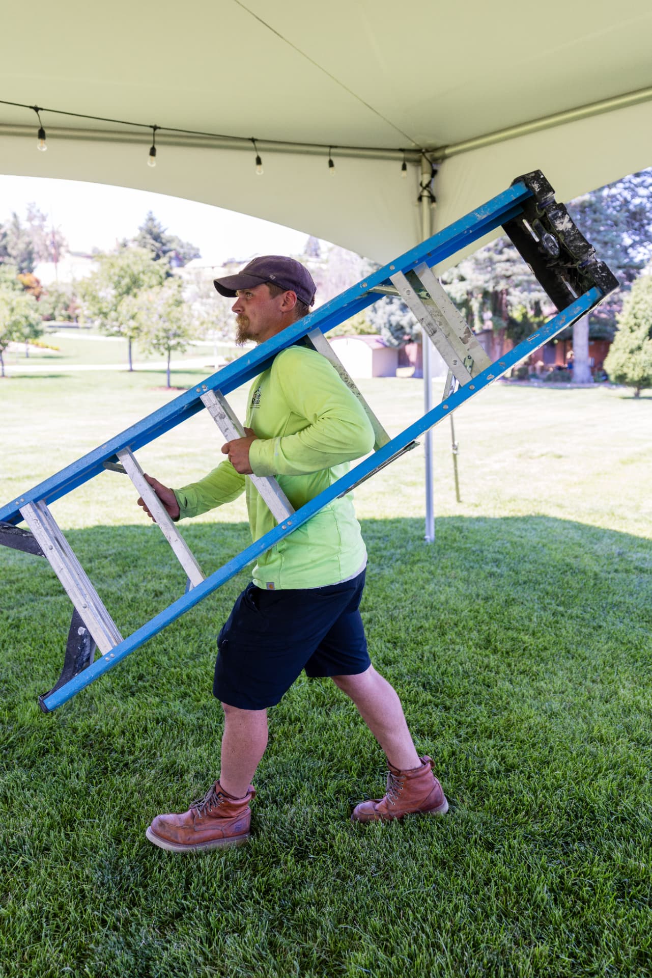 NCW Event Rentals crew member carrying a ladder under a high-peak tent during a Wenatchee Valley install