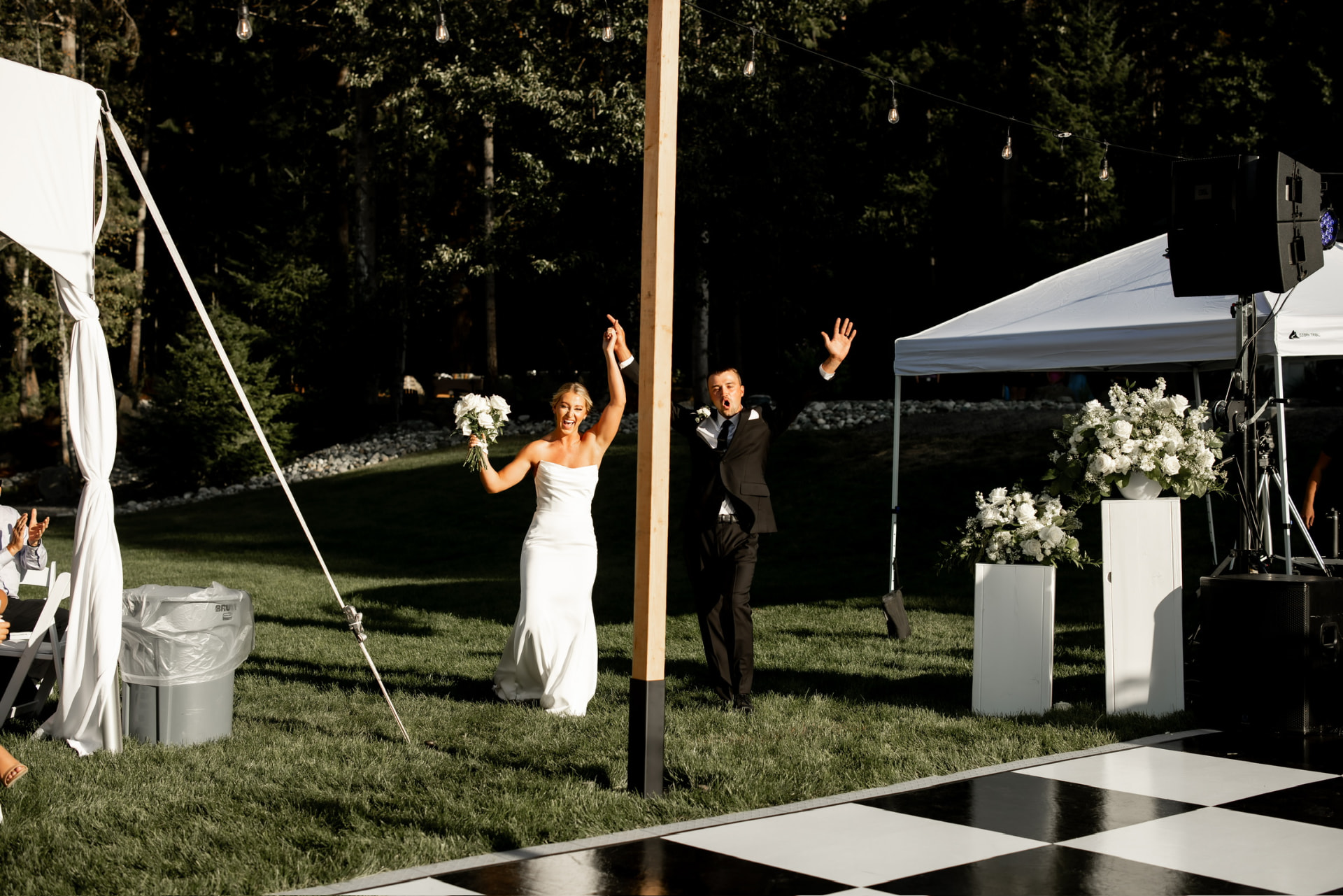 Bride and groom entering a checkered dance floor with string lights above at a forest wedding
