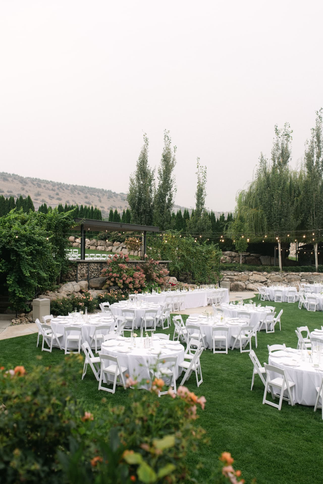 Round banquet tables with white linens and white folding chairs on a lawn reception in Eastern Washington