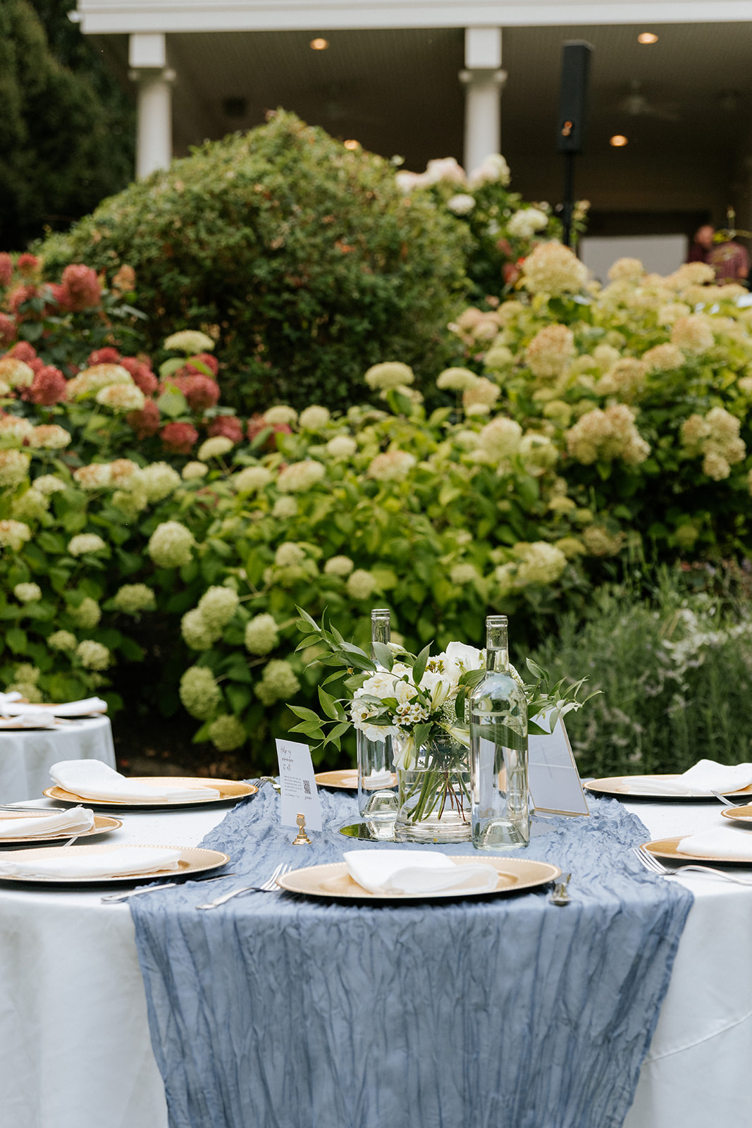 Reception table rental at Beecher Hill House in Wenatchee with white linen, dusty blue runner, gold chargers and a white garden floral centerpiece