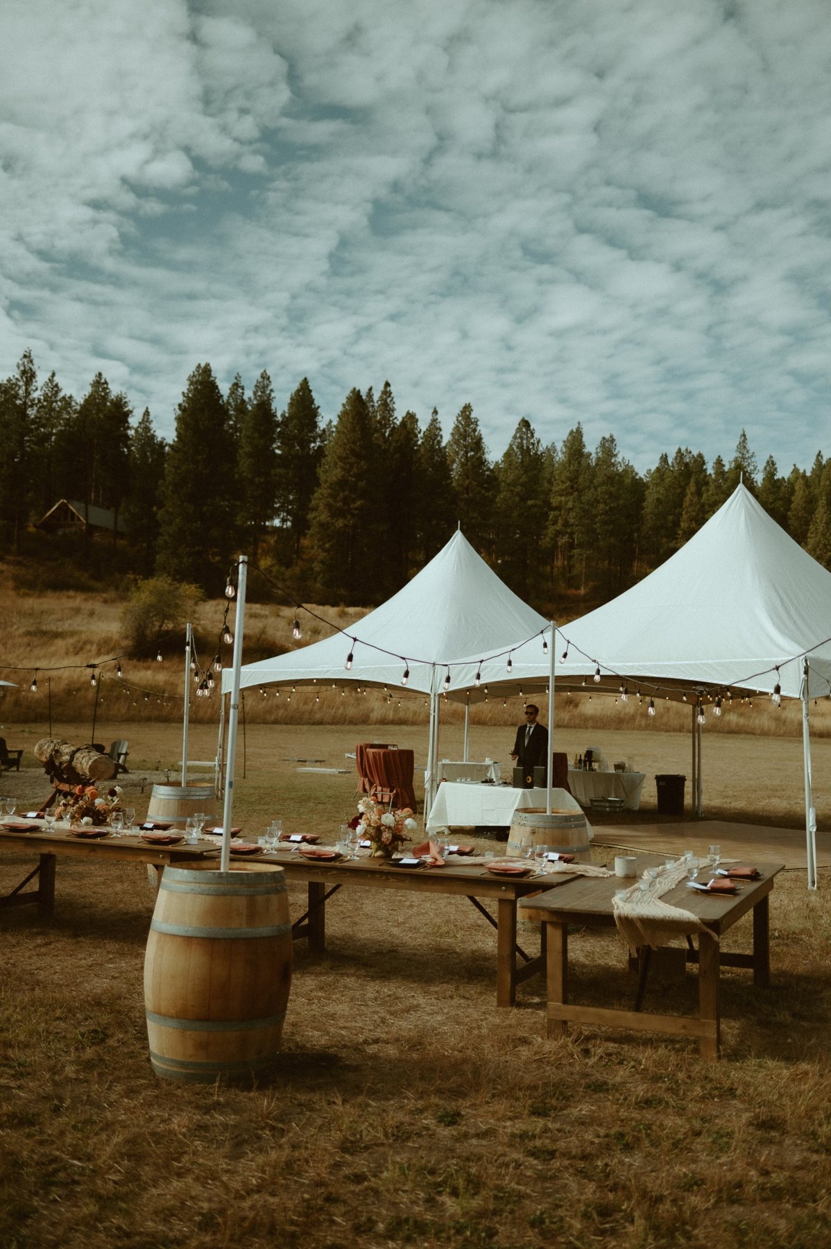Farmhouse tables with wine barrels, string lights and marquee tents at an outdoor Eastern Washington reception