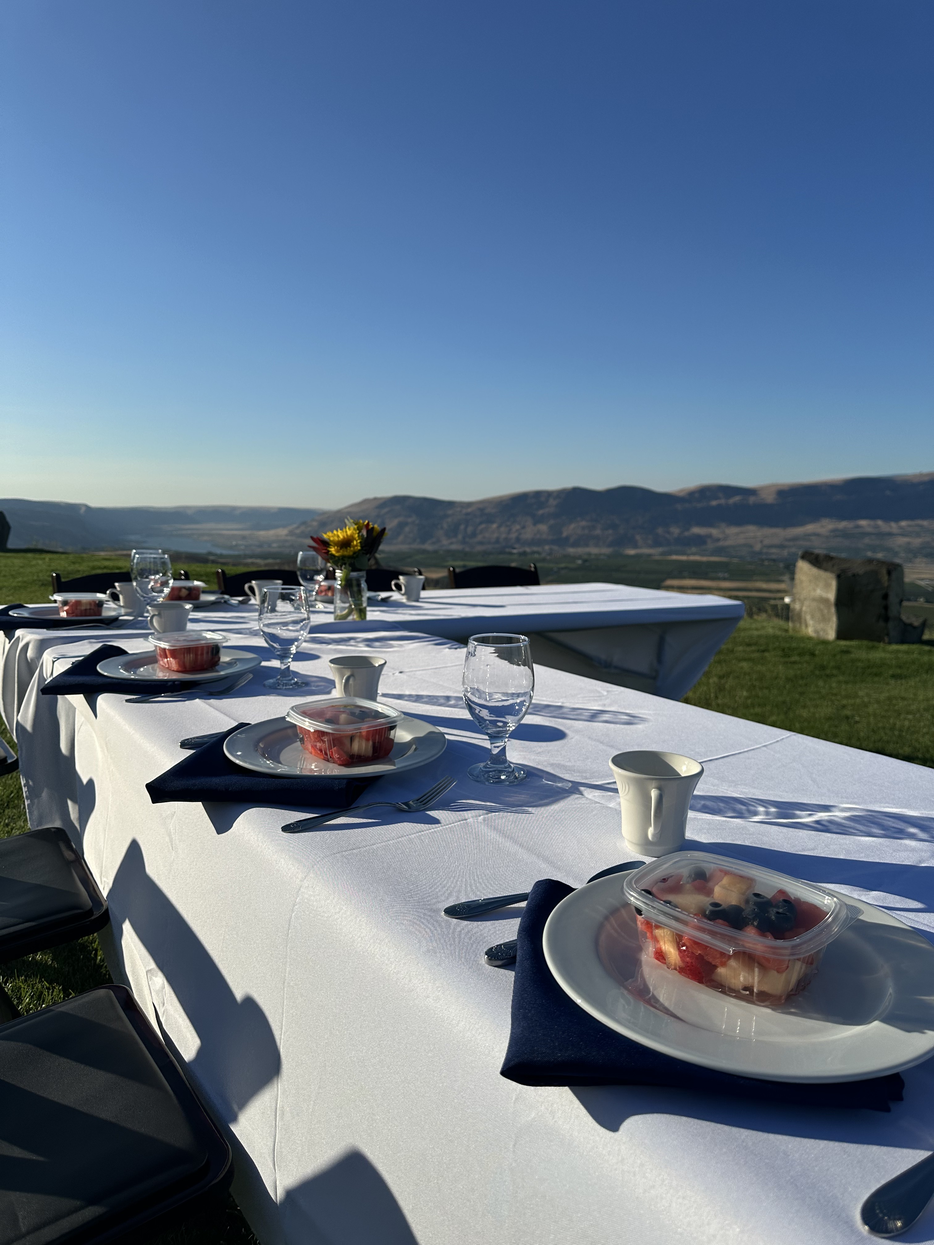 Black folding chair rentals at round tables with white linens, navy napkins and mountain views at an outdoor Eastern Washington wedding reception