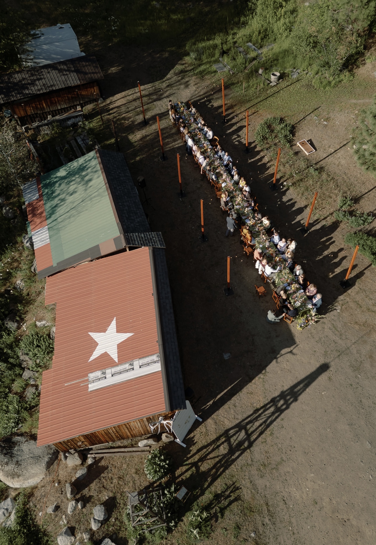 Drone photo of an outdoor reception with bistro string lights over a long dinner table beside a red barn with a white star on the roof in Eastern Washington