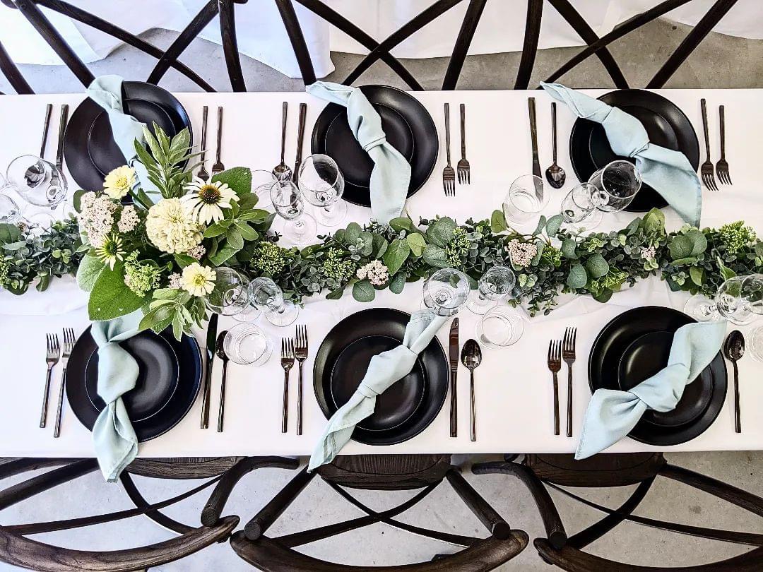Farm table set with black plates, bronze flatware rentals, sage green napkins and a eucalyptus garland runner in Eastern Washington