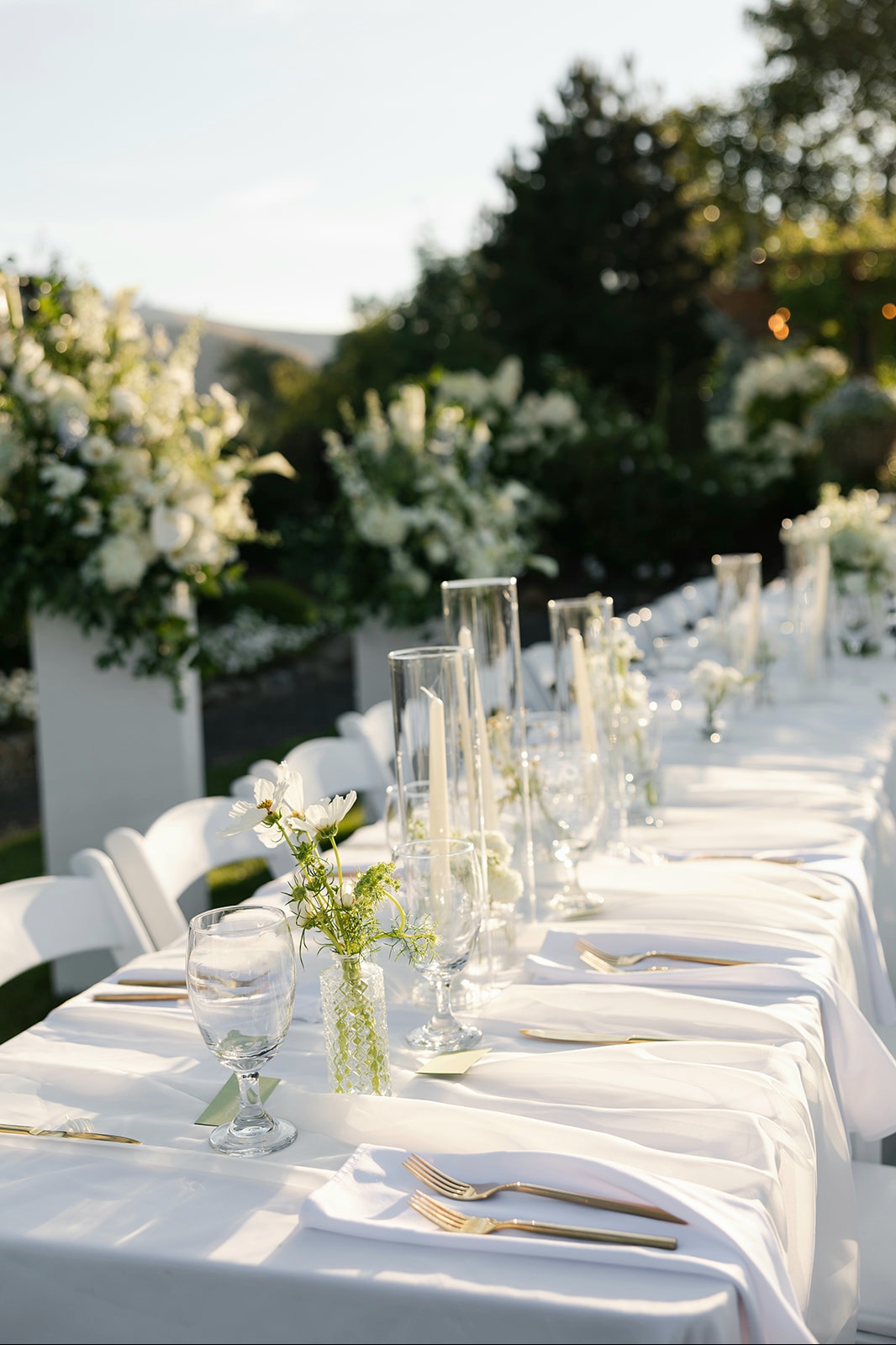 Banquet table rental with white linen, gold flatware, glassware and candle-and-flower centerpieces at a garden wedding reception in Eastern Washington
