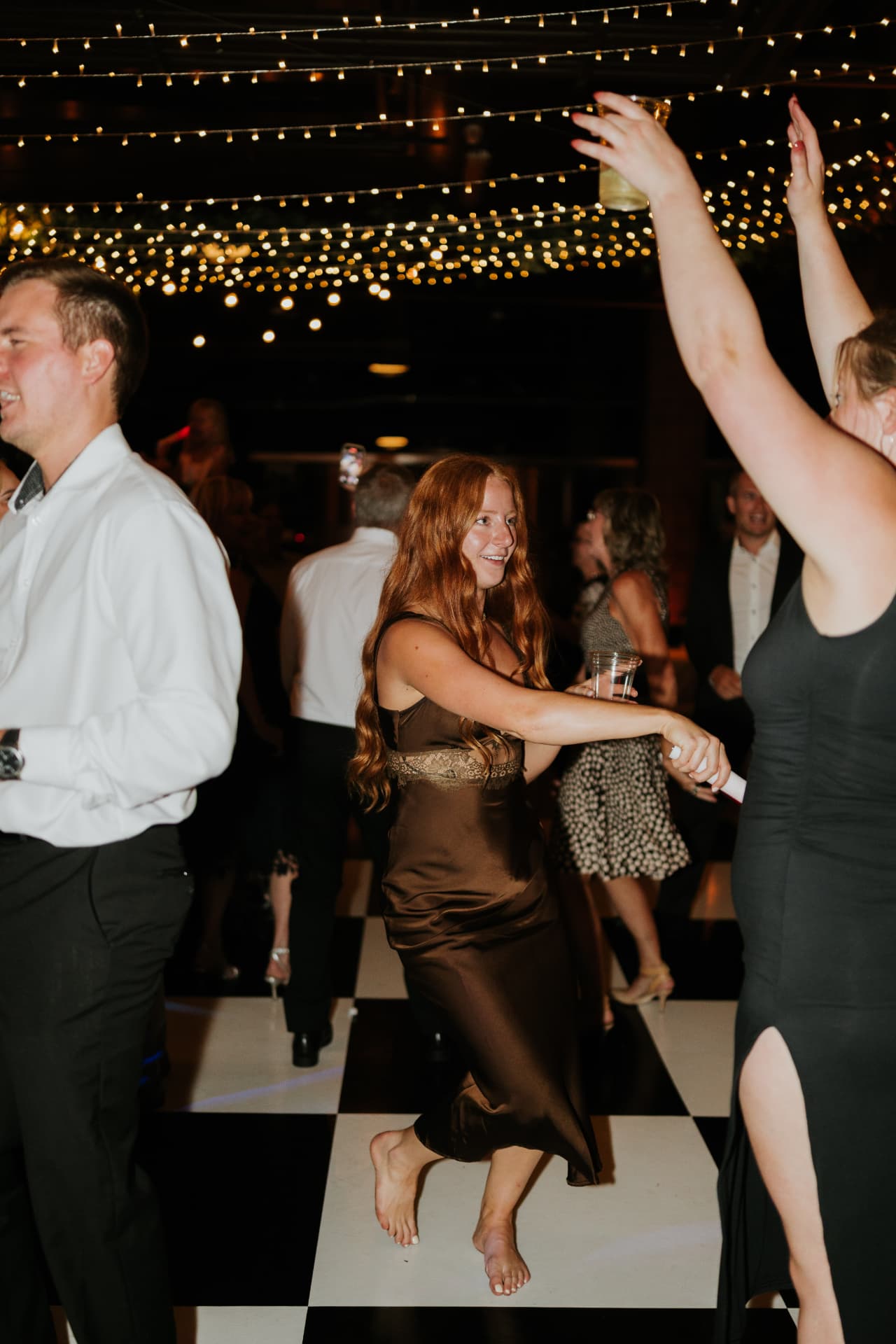 Wedding guests dancing the night away on a black and white checkered dance floor under warm string lights