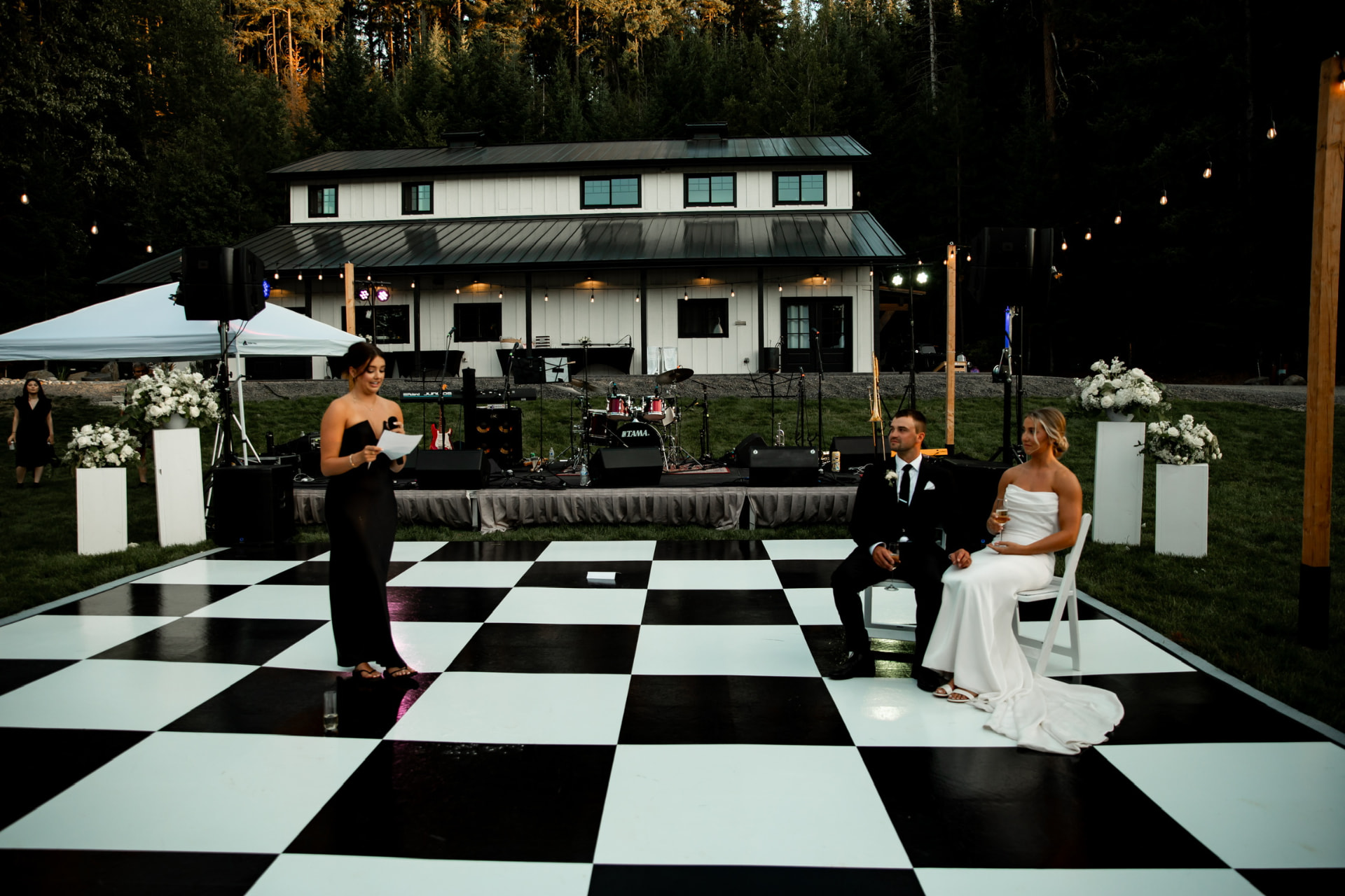 Outdoor wedding reception at White Barn Retreats near Cle Elum with a black and white checkered dance floor rented from NCW Event Rentals, string lights, and a white farmhouse backdrop