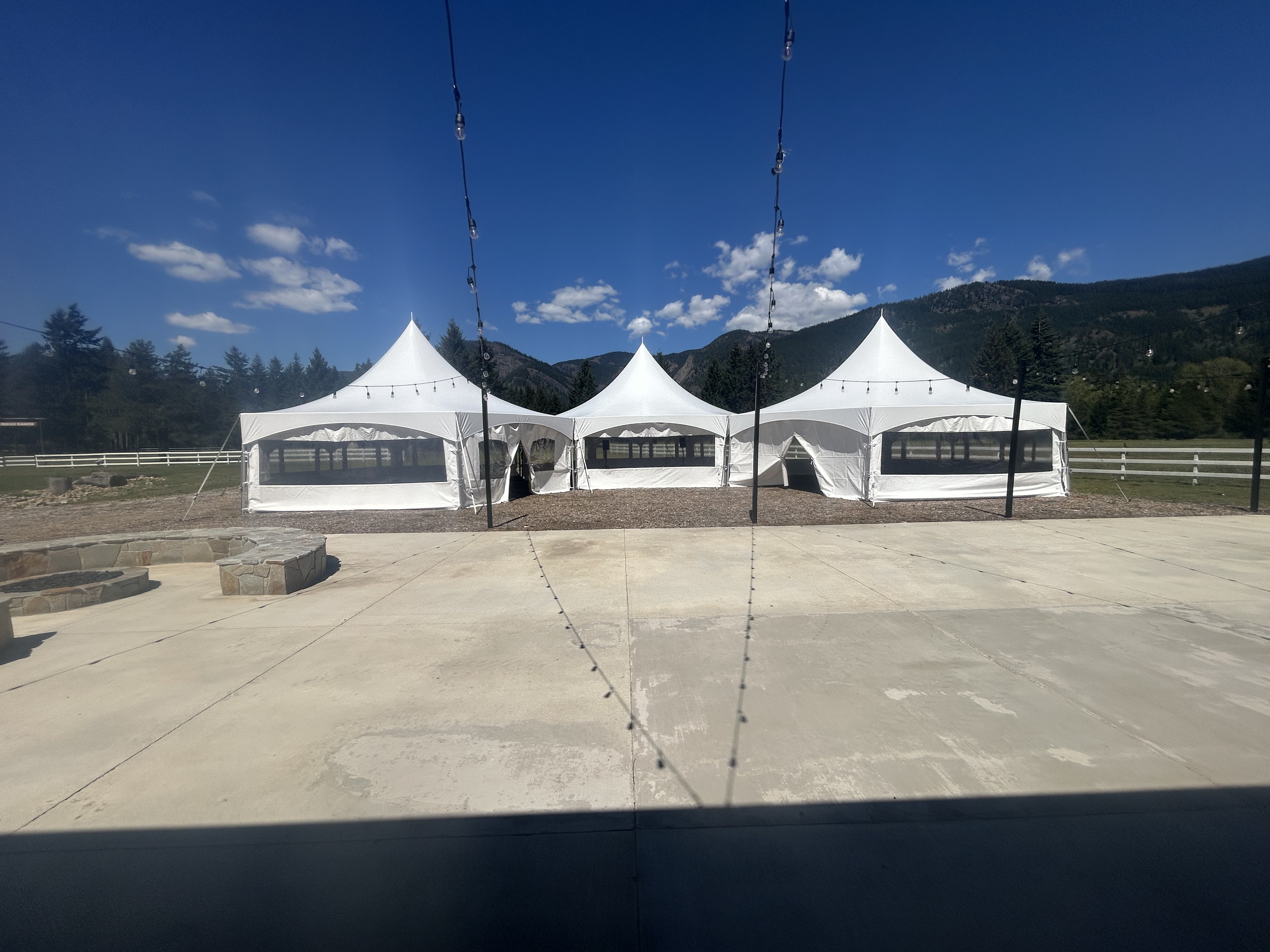 Three connected white high-peak tents with clear window sidewalls and string lighting installed on the patio at Silver Ridge Ranch near Cle Elum, Washington for a tent company corporate event