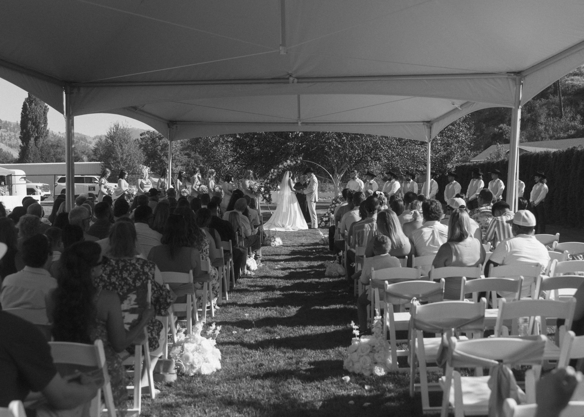Black and white photo of a wedding ceremony under a large white tent canopy with rows of white folding chair rentals facing the altar in Eastern Washington