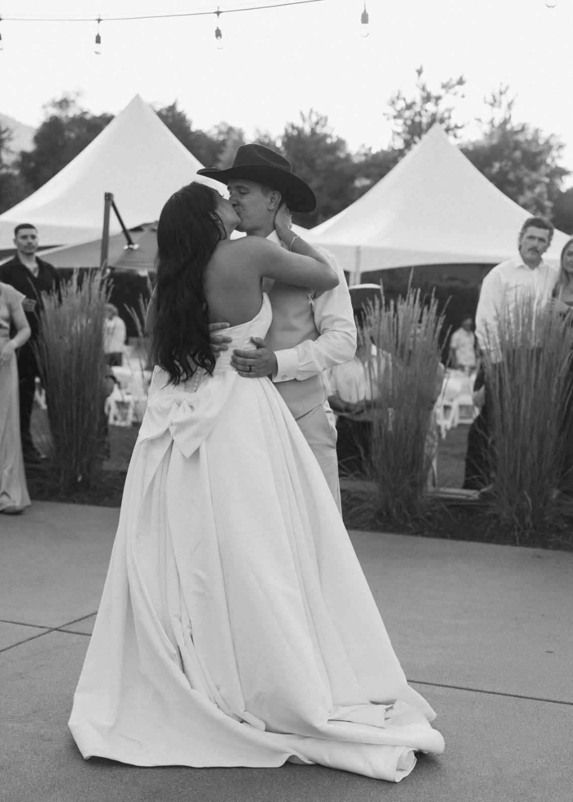 Black and white photo of a bride and groom kissing during their first dance in front of white high-peak tent rentals and string lights at an Eastern Washington wedding