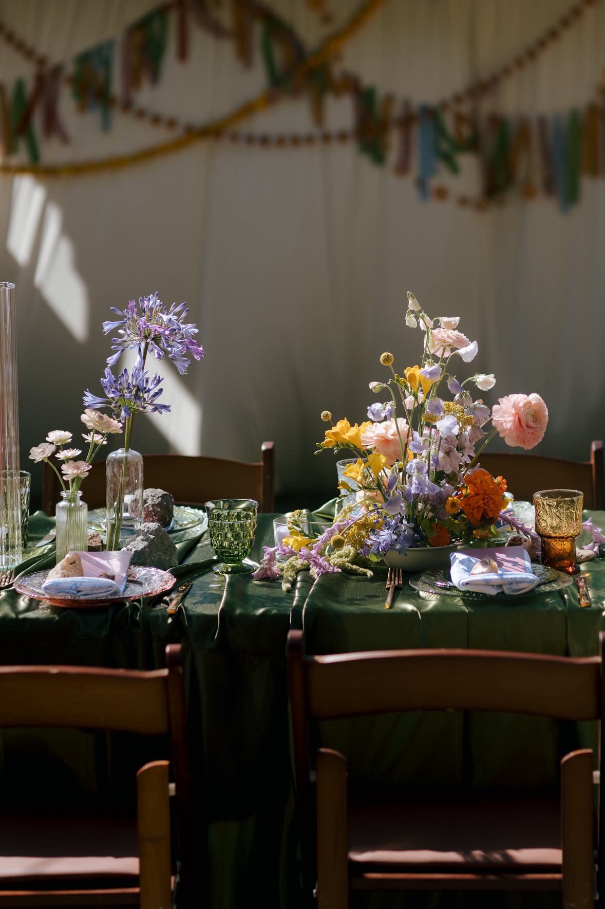 Wood folding chair rentals surrounding an emerald green reception table with colorful floral arrangements