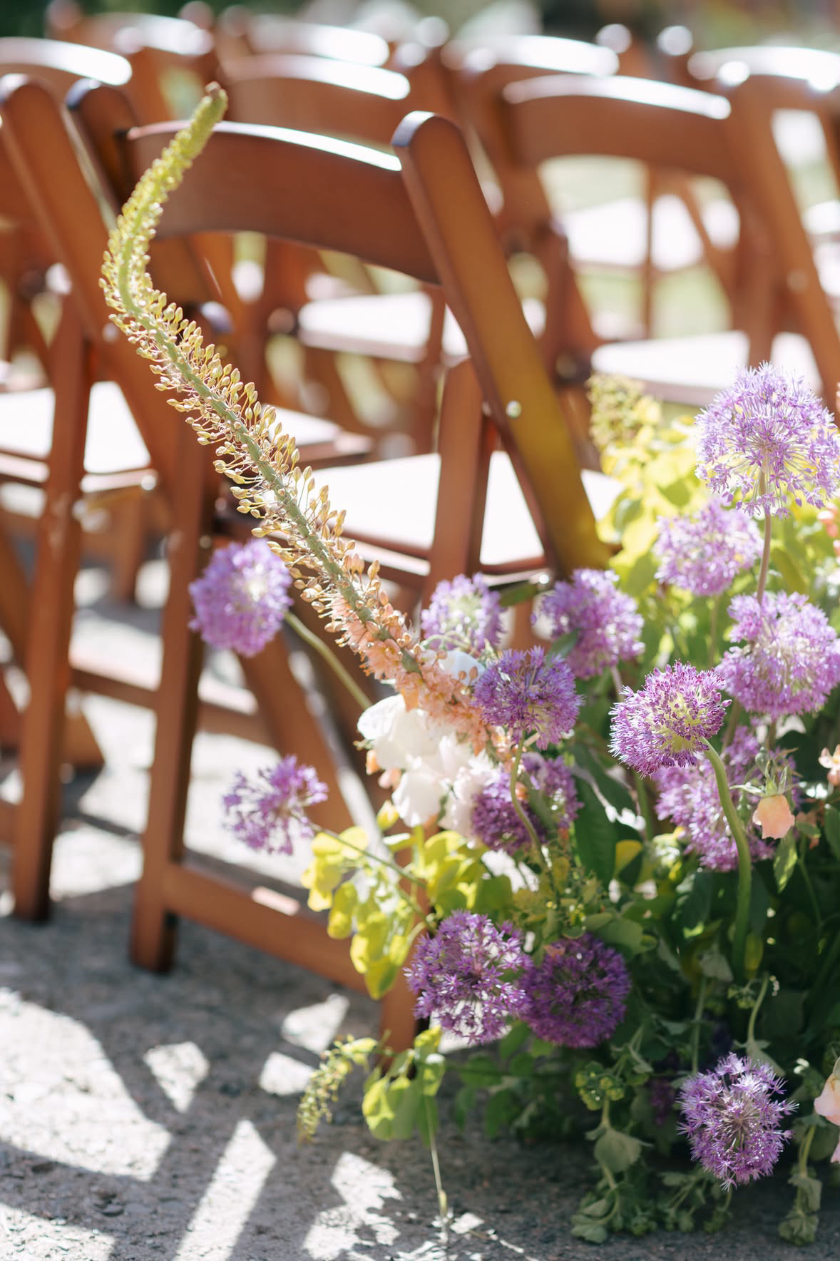 Rows of wood folding ceremony chairs beside purple and peach aisle flowers at a Eastern Washington wedding