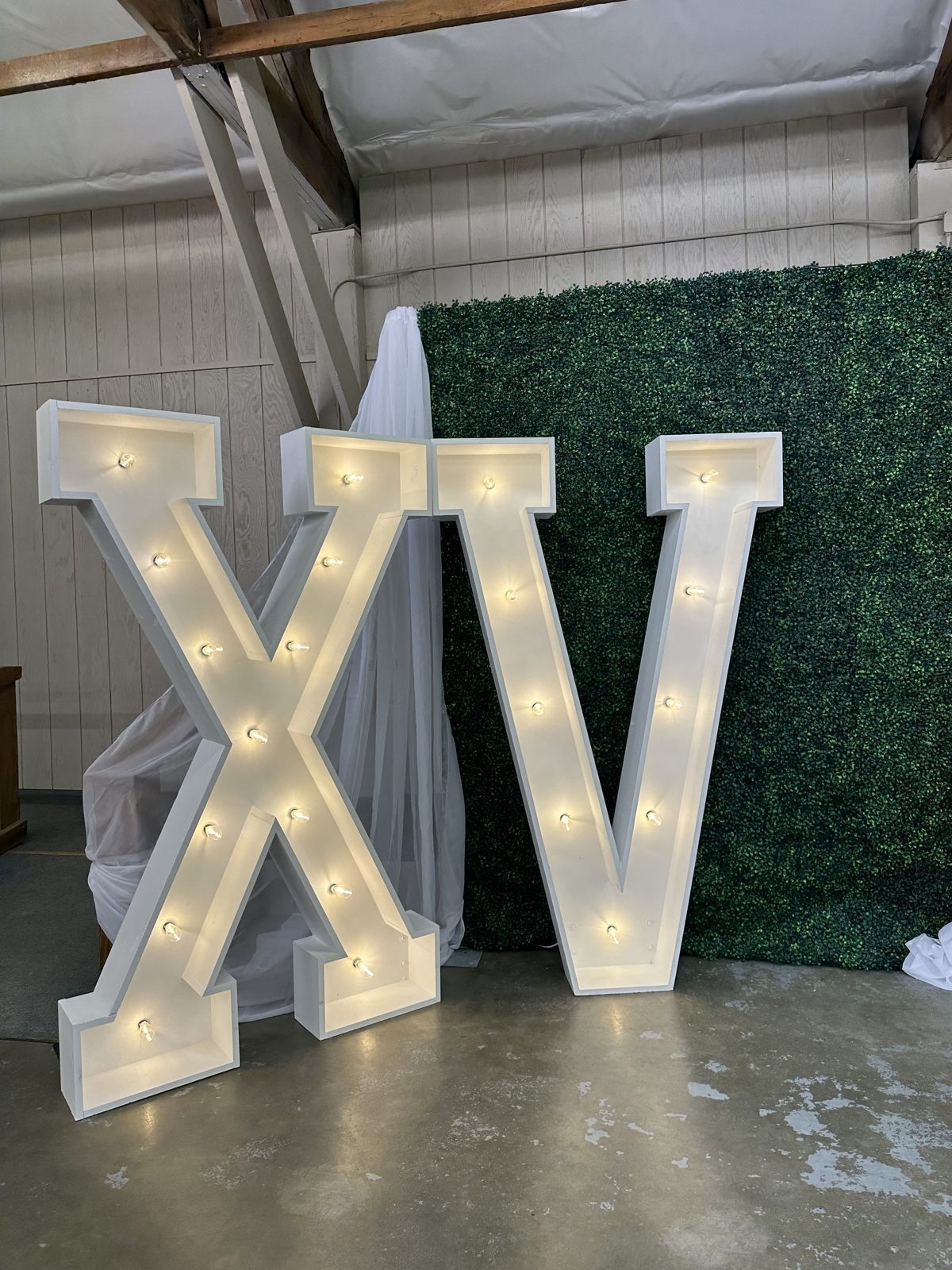 Giant lit XV marquee letters for a quinceañera set against a greenery wall