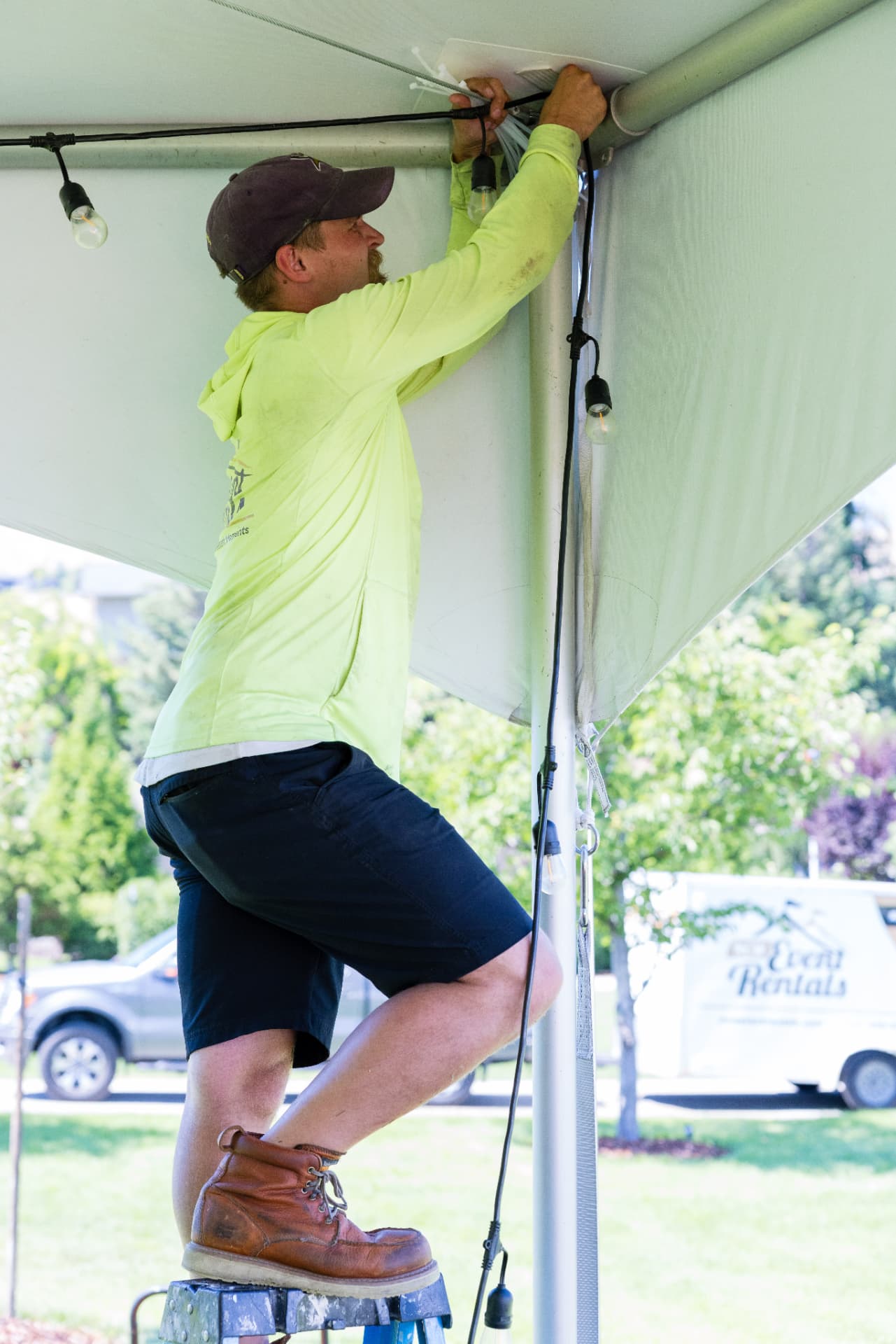 NCW Event Rentals installer hanging string lighting on a tent leg from a step stool