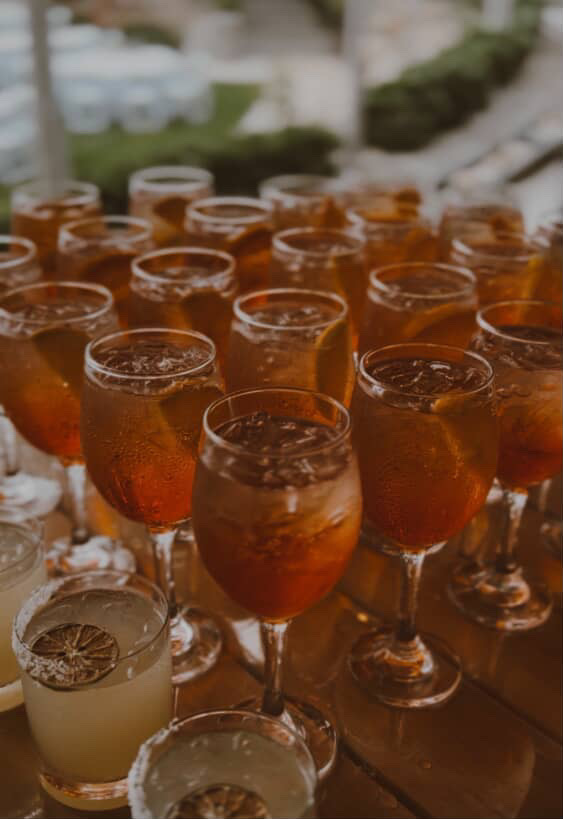 Wine glass rentals filled with Aperol spritz alongside margaritas in rocks glasses at an outdoor event bar