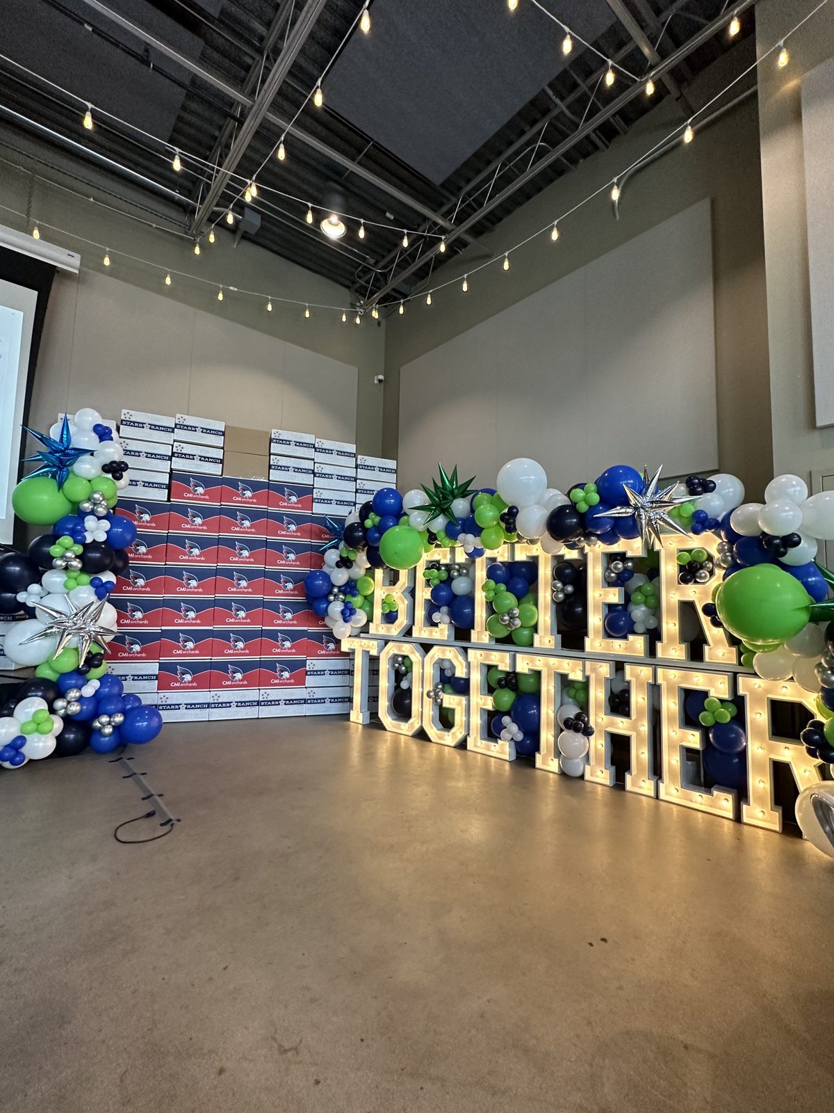 Large BETTER TOGETHER marquee letters framed by a balloon garland at a corporate celebration
