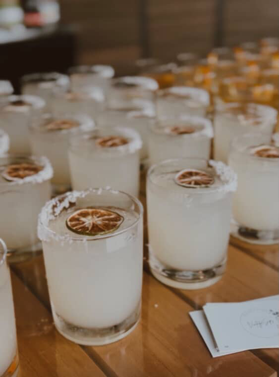 Salt-rimmed rocks glass rentals with margaritas and dried lime wheels lined up on a wood bar top