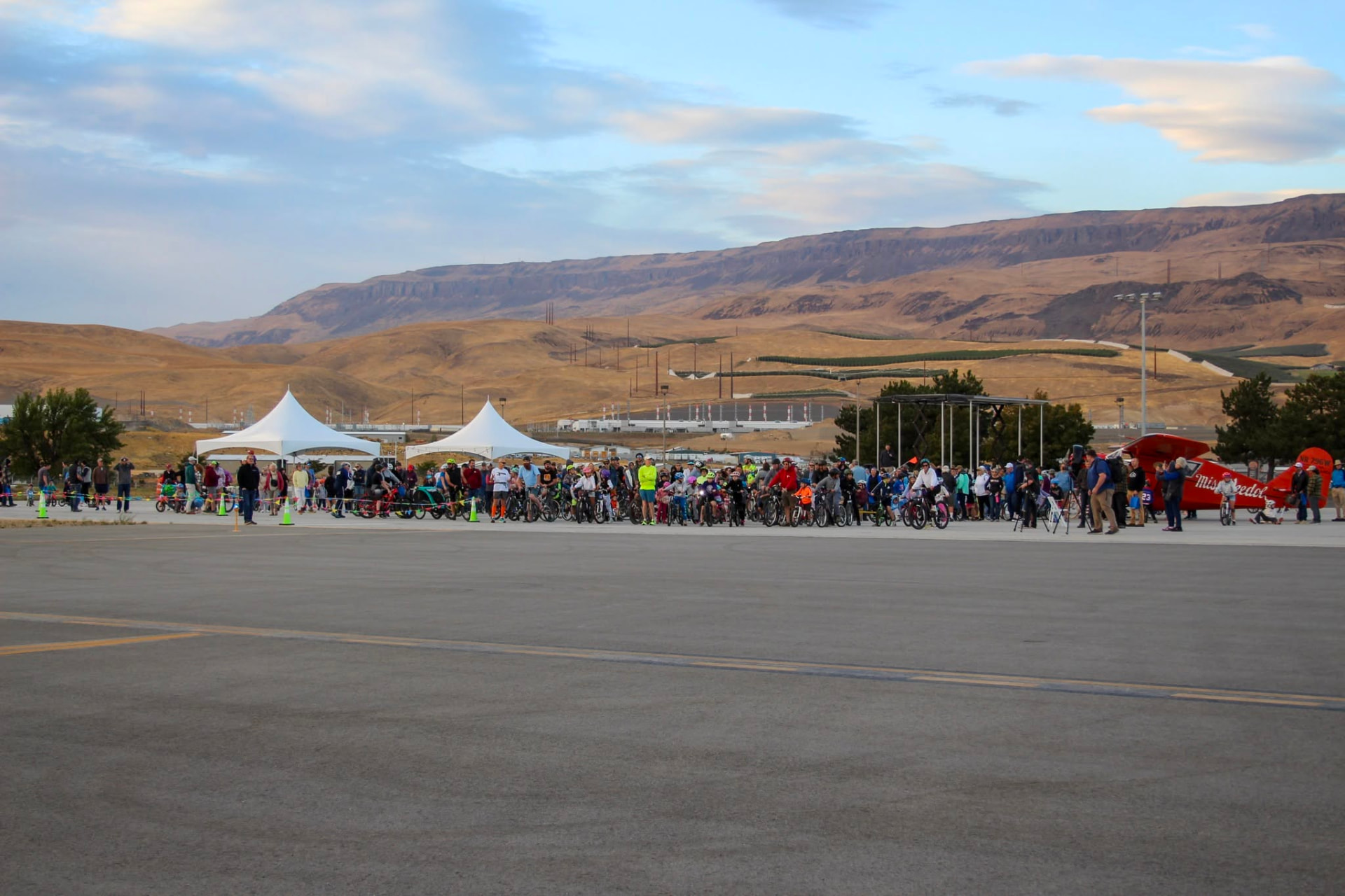 Two white high-peak tents on an airport tarmac with a large crowd gathered for a community terminal opening event in Eastern Washington
