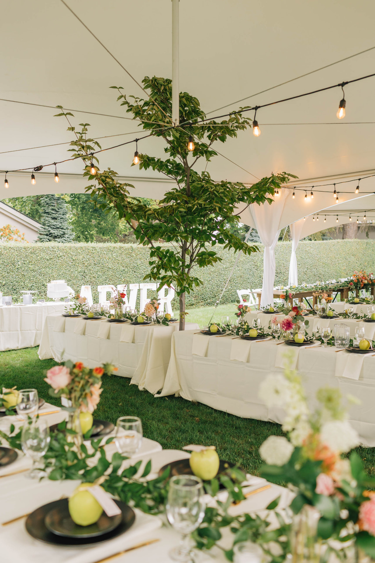 Gold flatware rentals with black charger plates and water goblets on ivory linens at a tented reception in Eastern Washington