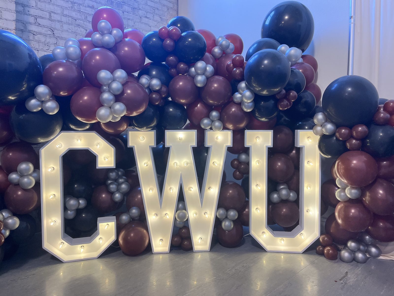 Illuminated CWU marquee letters in front of a navy and maroon balloon garland at a Central Washington University event