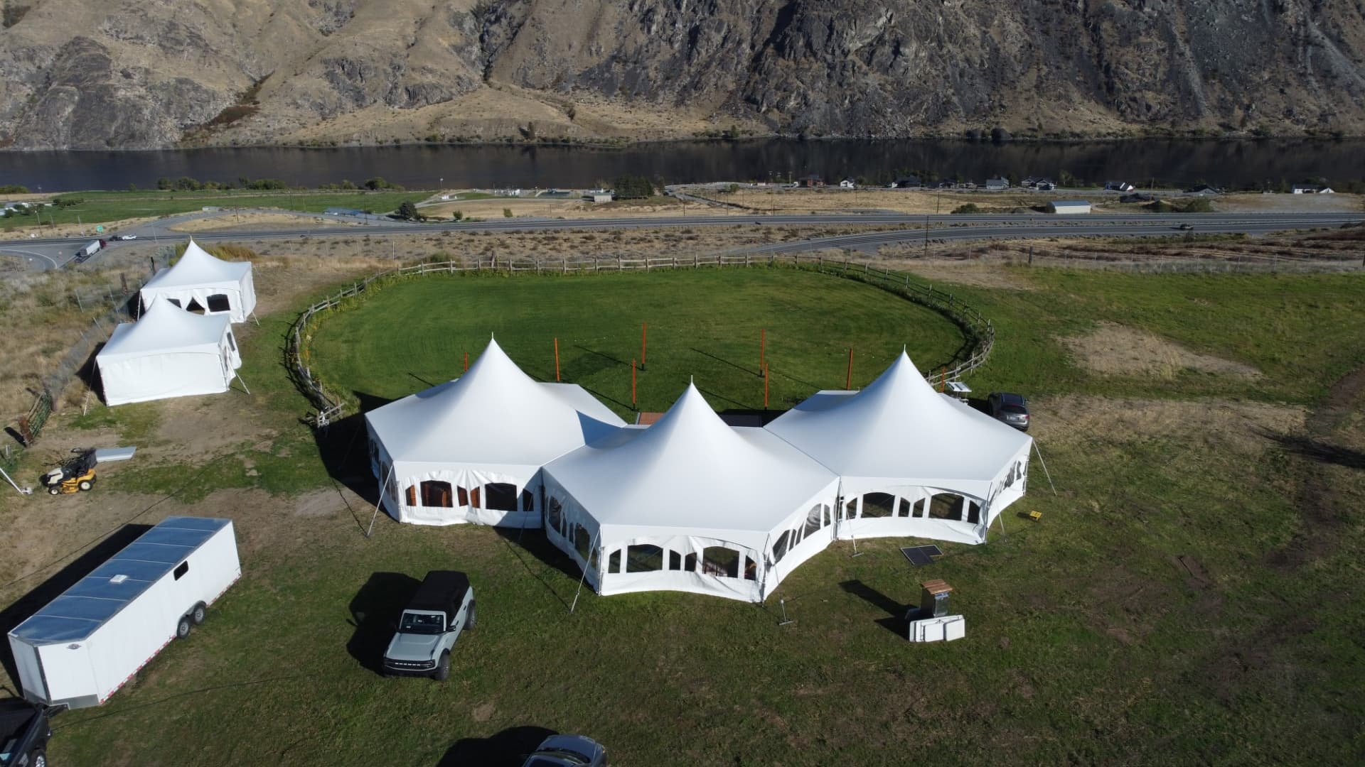 Angled aerial drone view of three connected high-peak hexagon tents at a Chelan wedding on private property — 3 Hex Tent Crescent Package with bride and groom's suite, dance floor and custom courtyard lighting from NCW Event Rentals