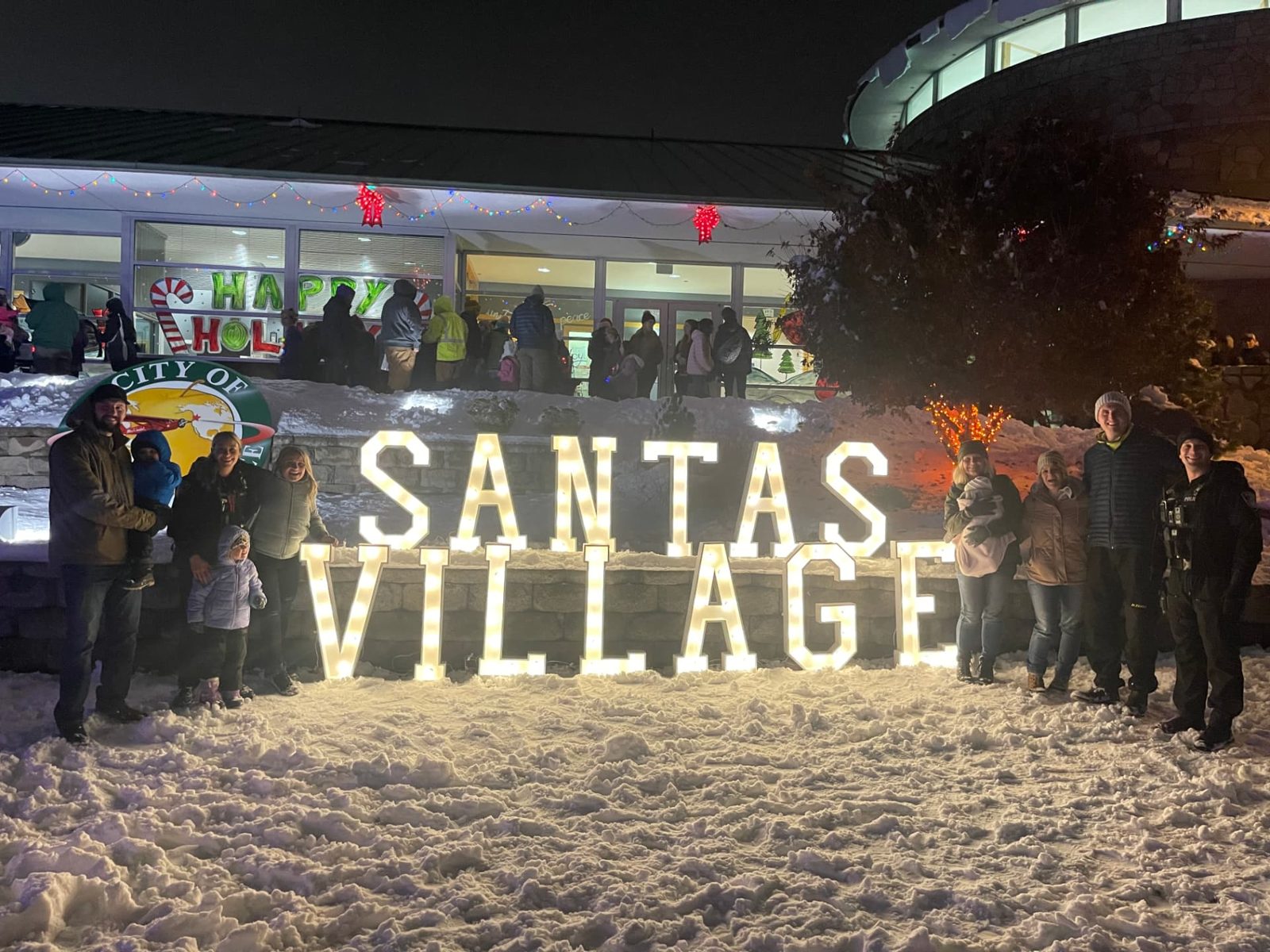 Lit SANTAS VILLAGE marquee letters in the snow with families gathered at a community holiday event in Eastern Washington