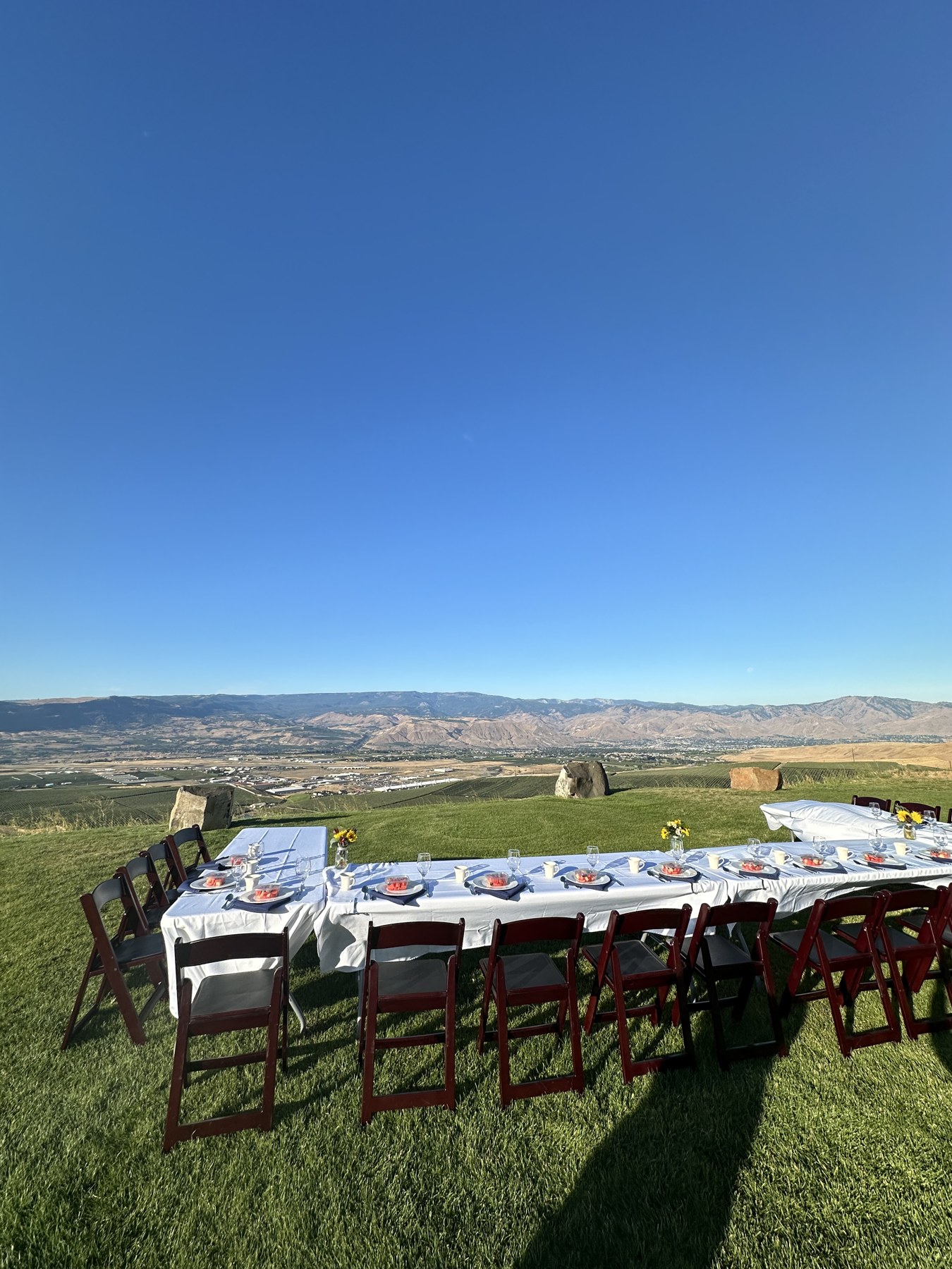 Long banquet table rows set with china and glassware on a ridge above Wenatchee at sunrise