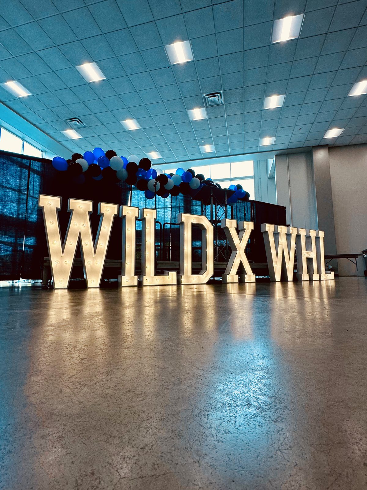 Lit marquee letters spelling WILD X WHL at a corporate hockey partnership event