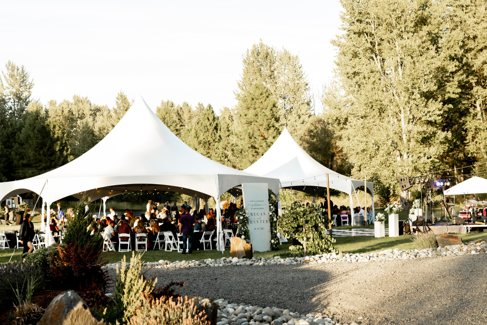 Two connected white high-peak wedding tents with string lights, white folding chairs and a stage at a private property wedding in Eastern Washington