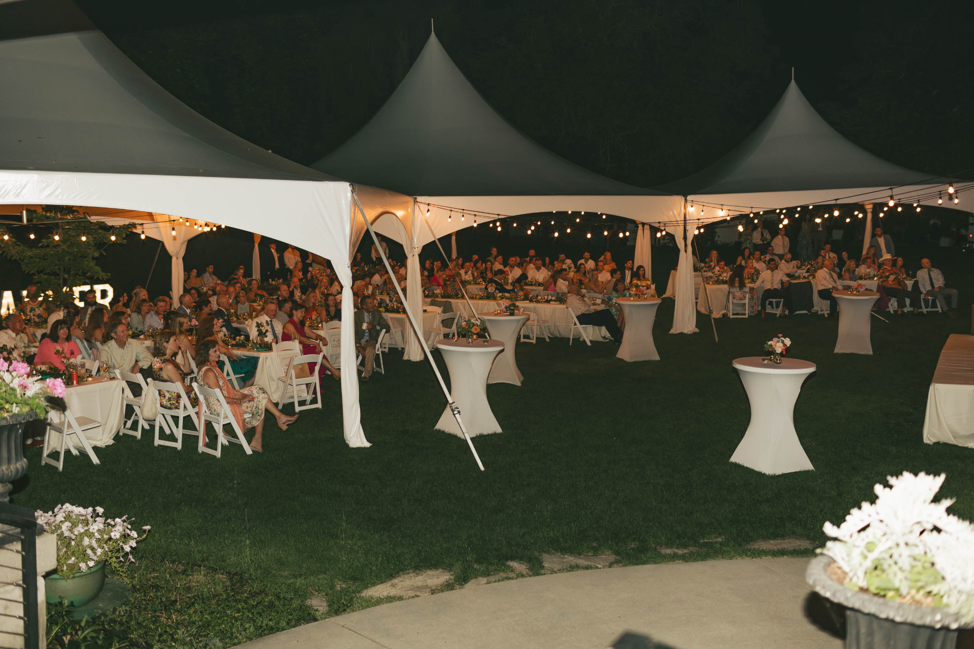 Reception rounds and white spandex-covered cocktail tables under bistro-lit pole tents at a nighttime Eastern Washington wedding
