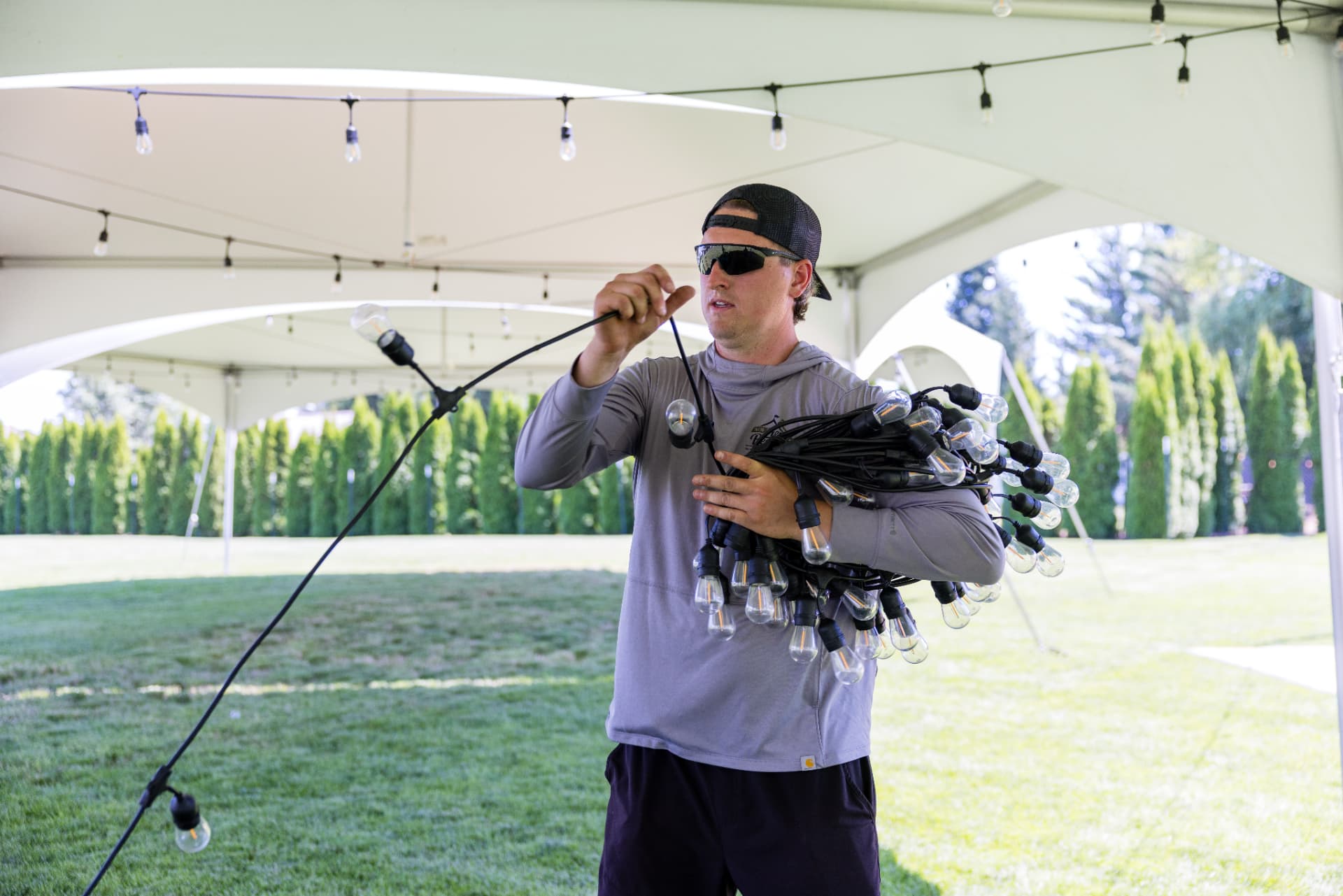 Crew member unspooling a strand of bistro string lights inside a white event tent