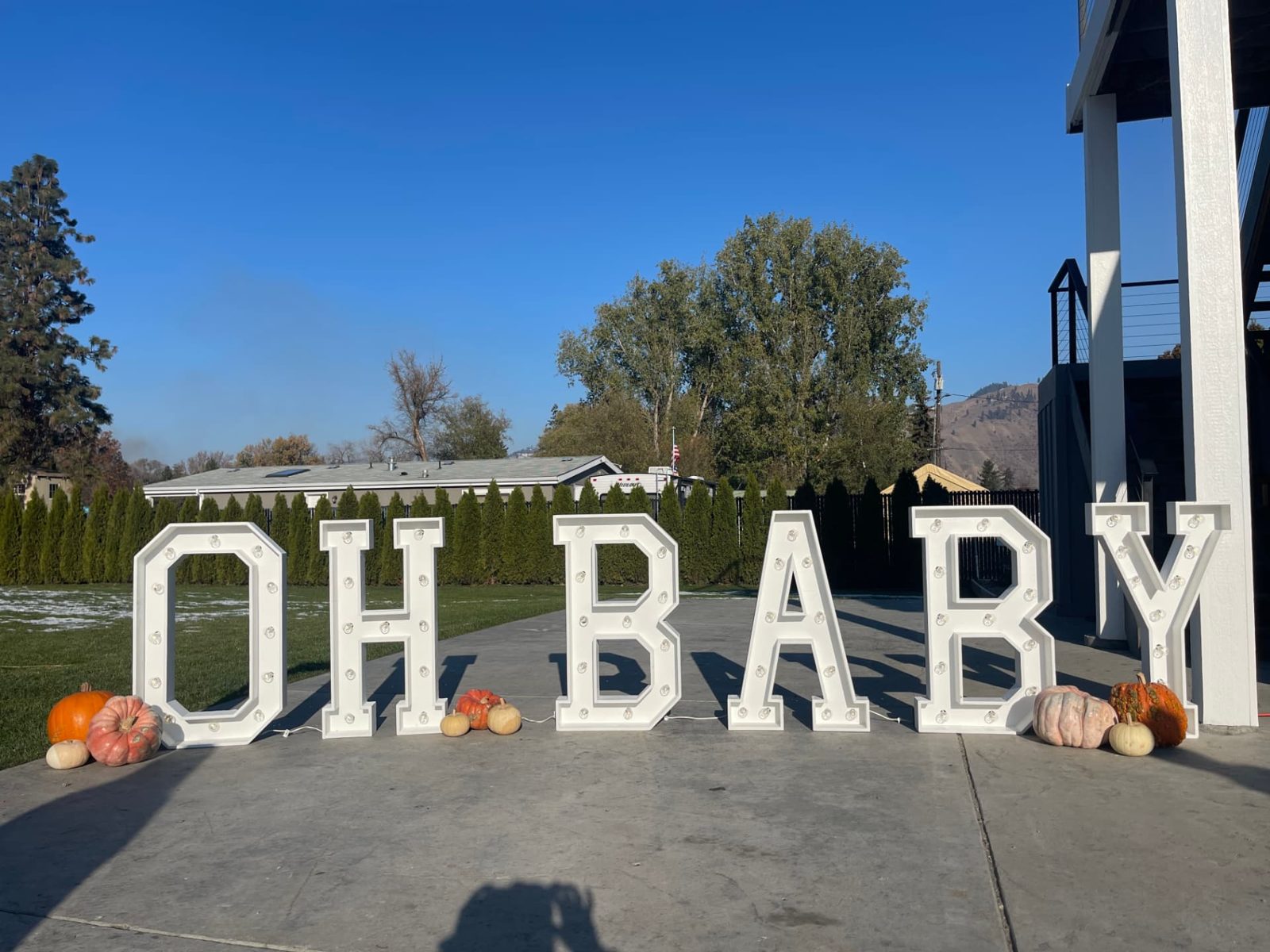 White OH BABY marquee letters set up outdoors with fall pumpkins under a blue sky at an Eastern Washington baby shower