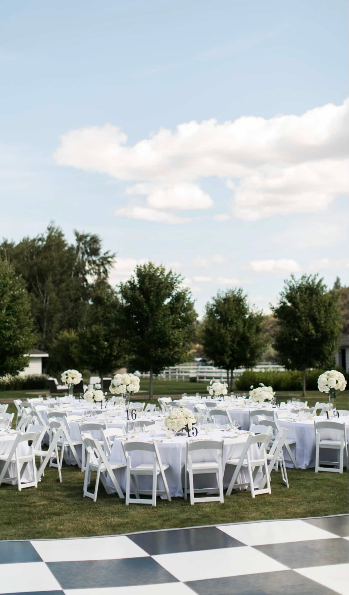 White resin folding chairs around white-linen round tables beside a black and white checkered dance floor