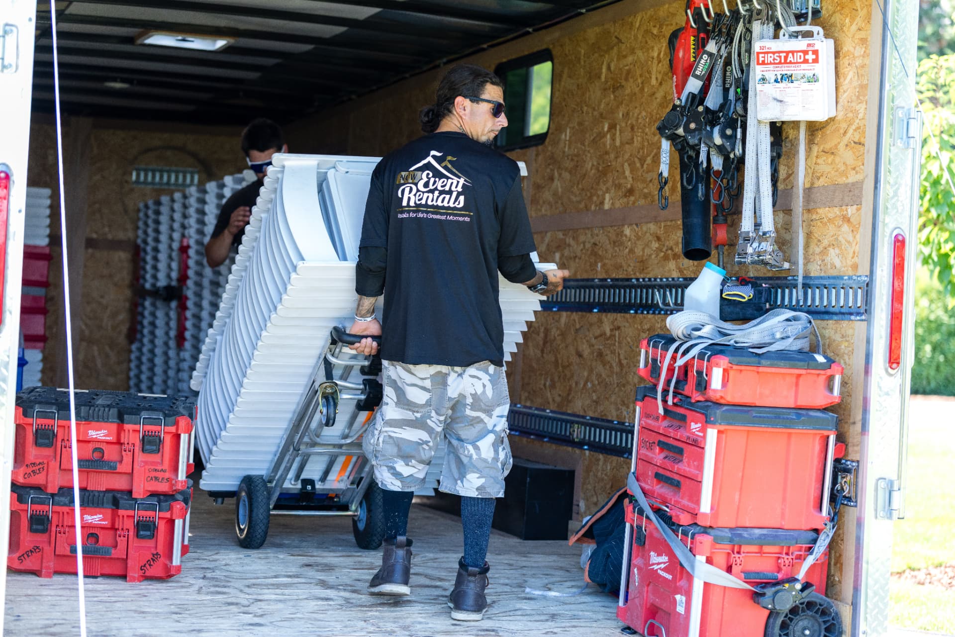 NCW Event Rentals team loading stacks of white folding chairs into a delivery trailer